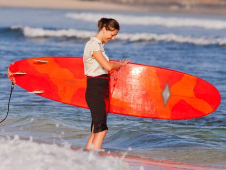 Businesswoman holding a surf board on the beach in the water