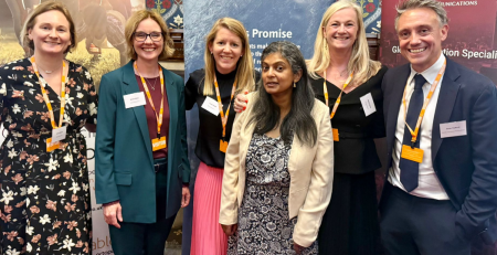 Group of five women and one man posing for photo in front of three standup banners with details (mostly obscured) of MD Communications, Parents Promise and amicable. They are smiling, dressed in business casual clothing and wearing orange lanyards.