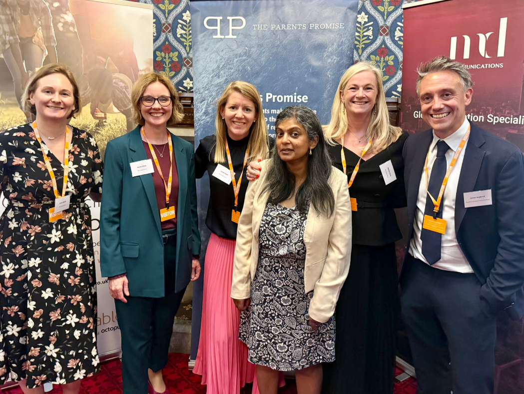 Group of five women and one man posing for photo in front of three standup banners with details (mostly obscured) of MD Communications, Parents Promise and amicable. They are smiling, dressed in business casual clothing and wearing orange lanyards.