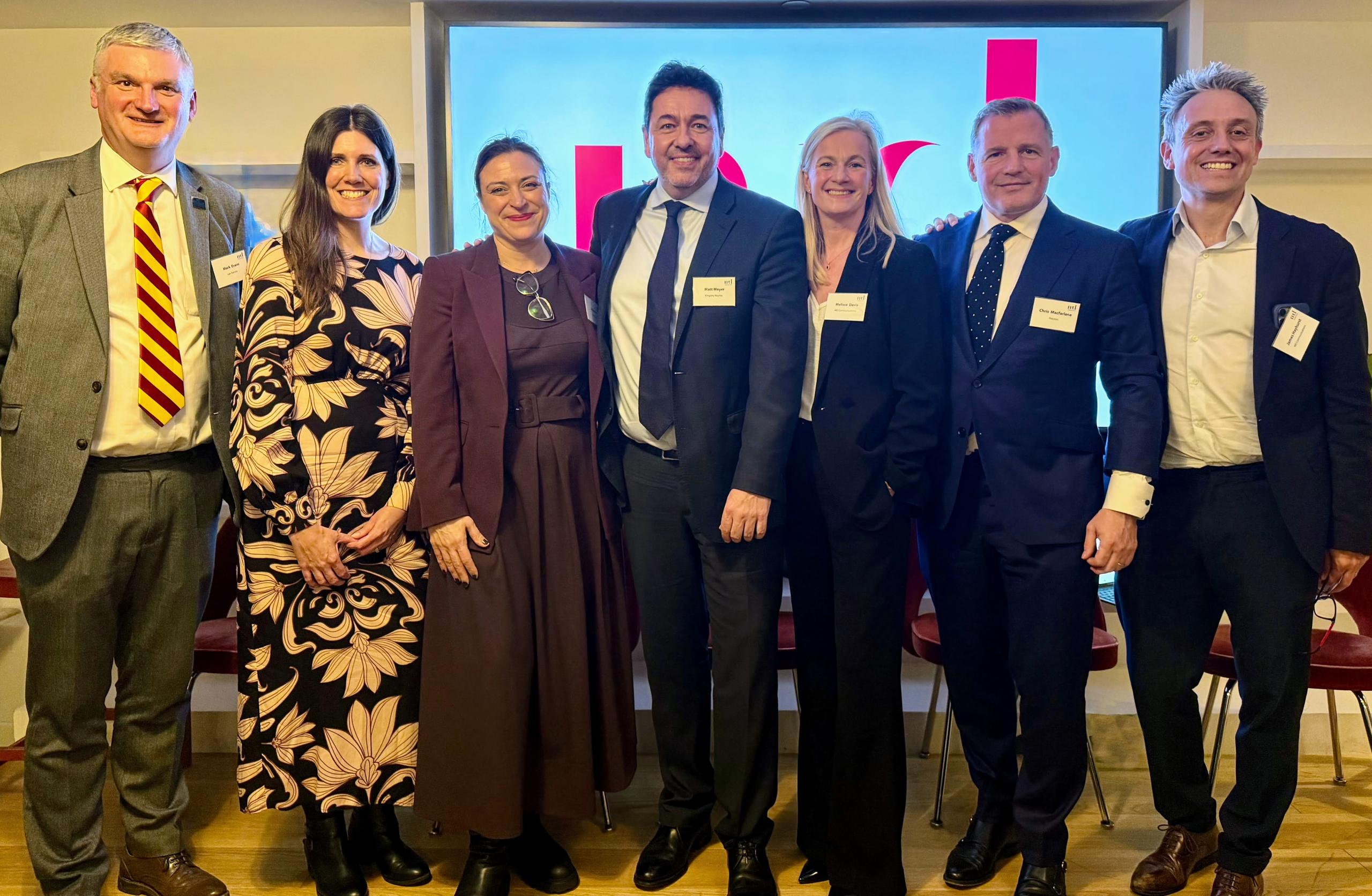 purpose event panel - group of four men and three women standing in front of obscured MD Comms logo on big screen, in front of chairs, at 180 Strand